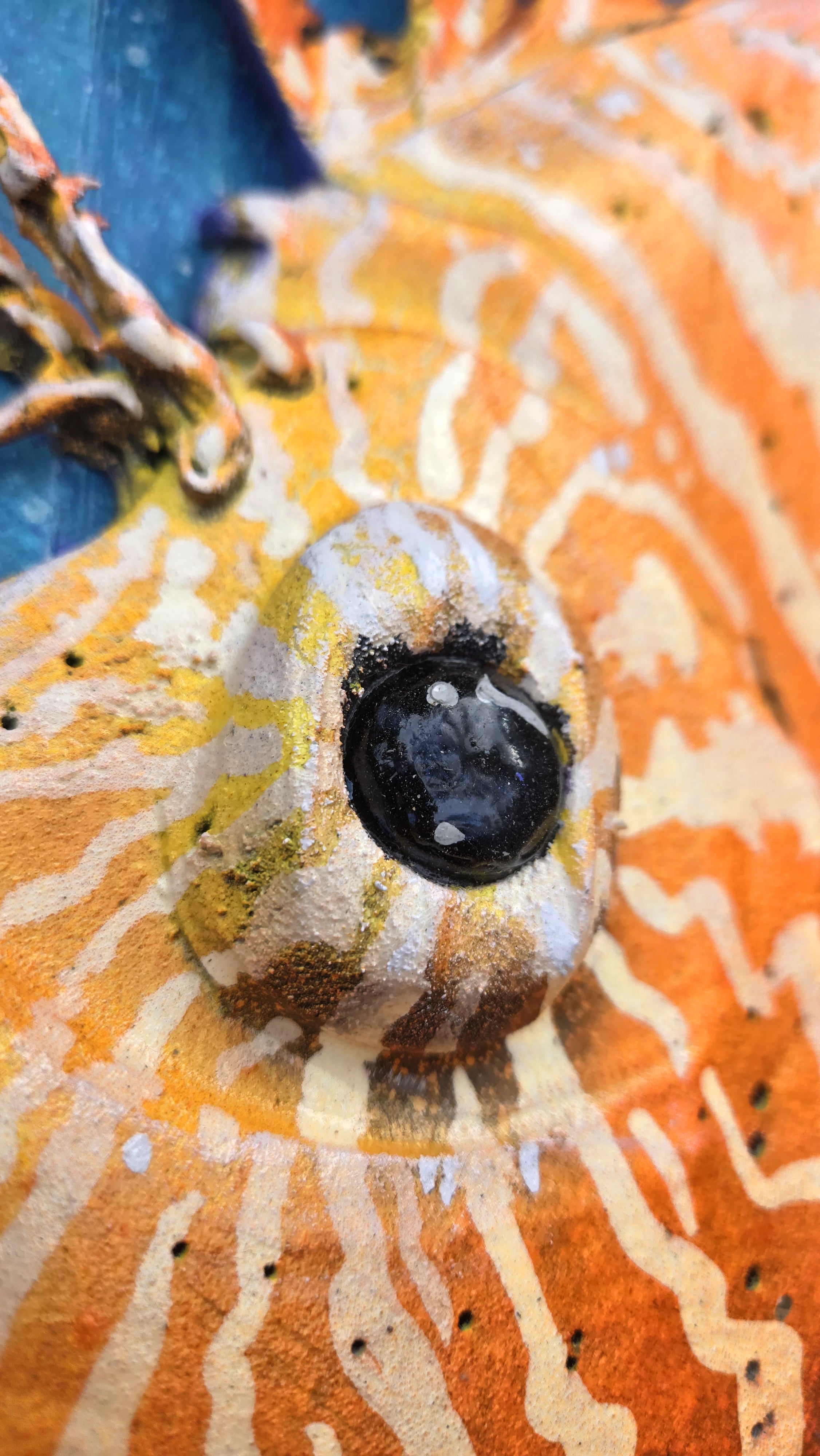 A close-up of a handcrafted Lion Fish with a prominent black eye detail, featuring orange, white, yellow, and blue colors.
