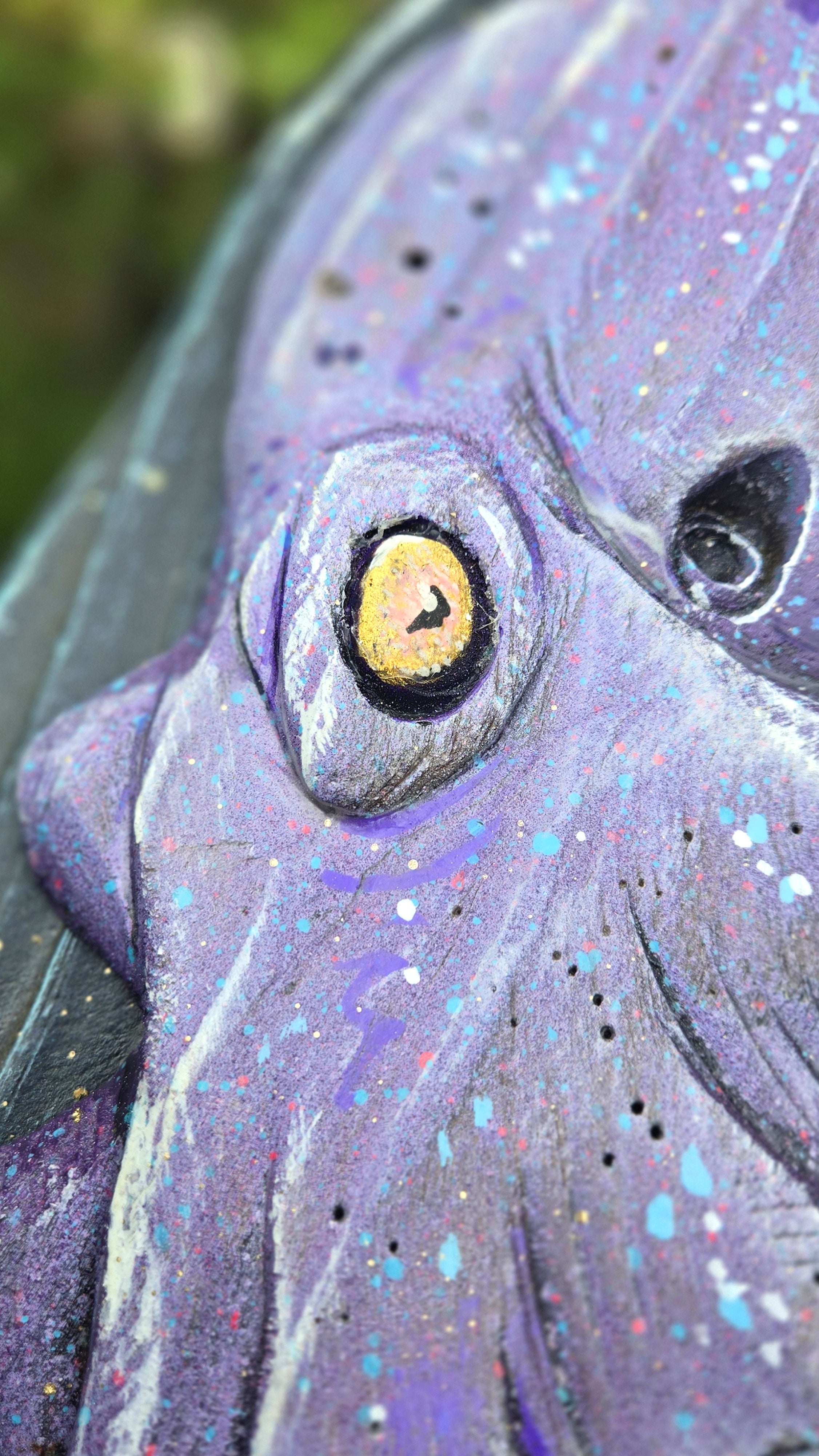 Extreme close-up of a handcrafted  Octopus face with a large yellow eye, dark pupil, and textured purple surface with paint splatters.