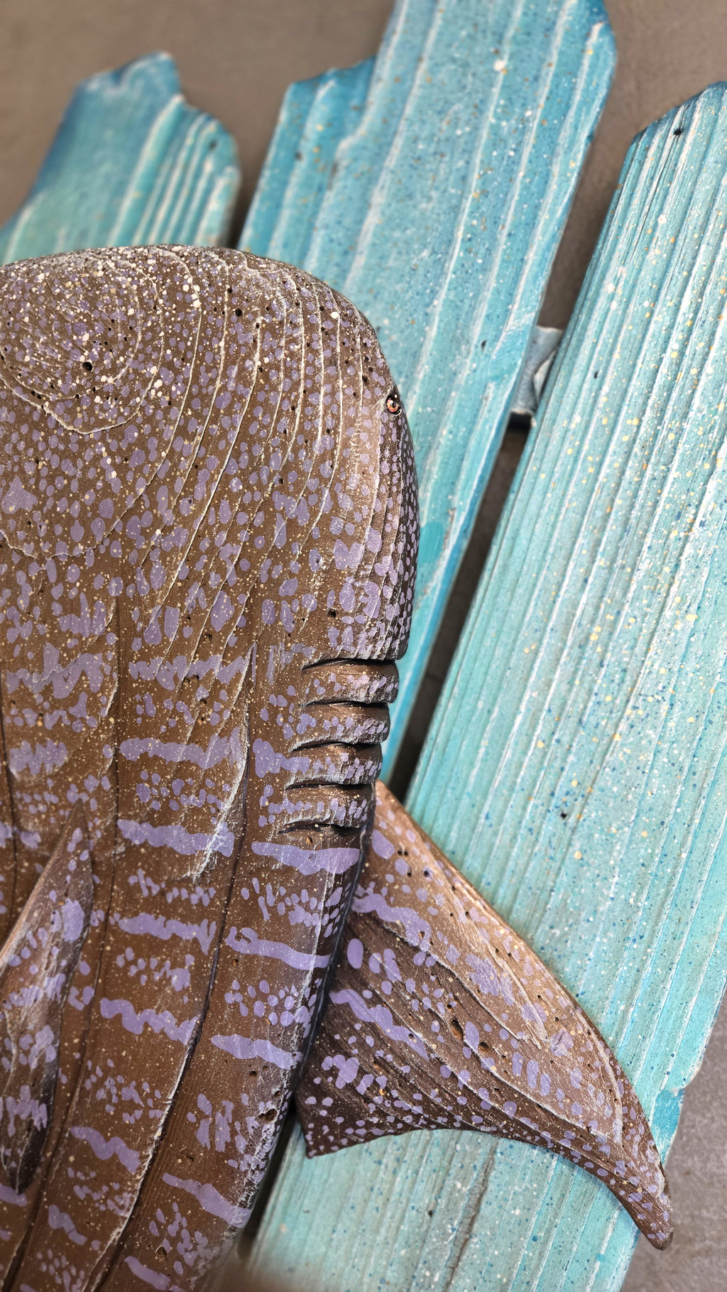 A close-up of a decorative whale shark wall art piece mounted on a distressed turquoise wooden pallet frame.