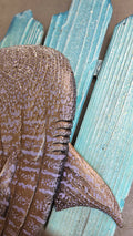 A close-up of a decorative whale shark wall art piece mounted on a distressed turquoise wooden pallet frame.