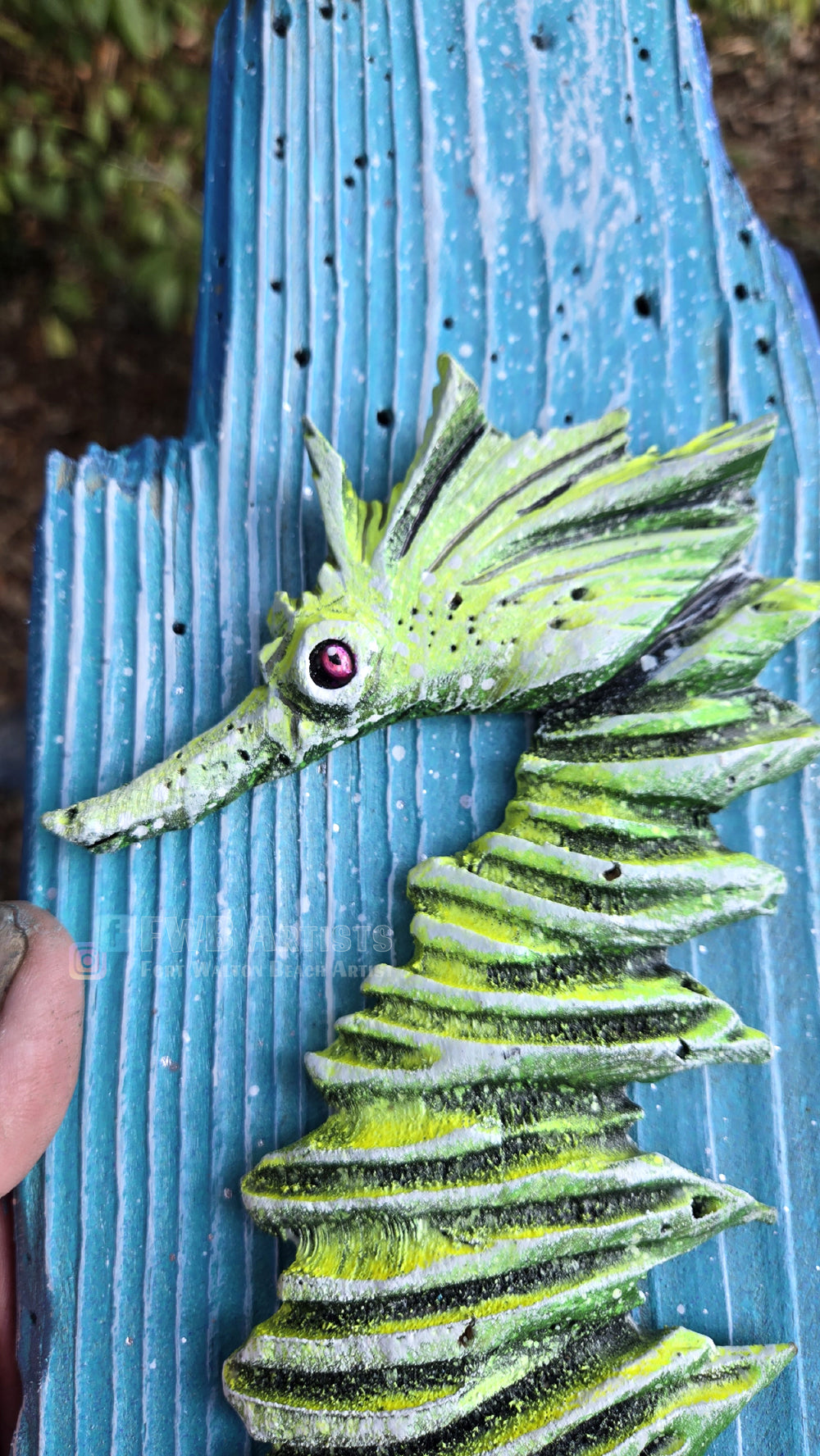 A close up of a hand carved, hand-painted wooden wall art piece featuring a green seahorse on a weathered light blue background. Handmade, one-of-a-kind up-cycled Eco-Art from locally reclaimed materials Thomas Walsh at FWB Artists.