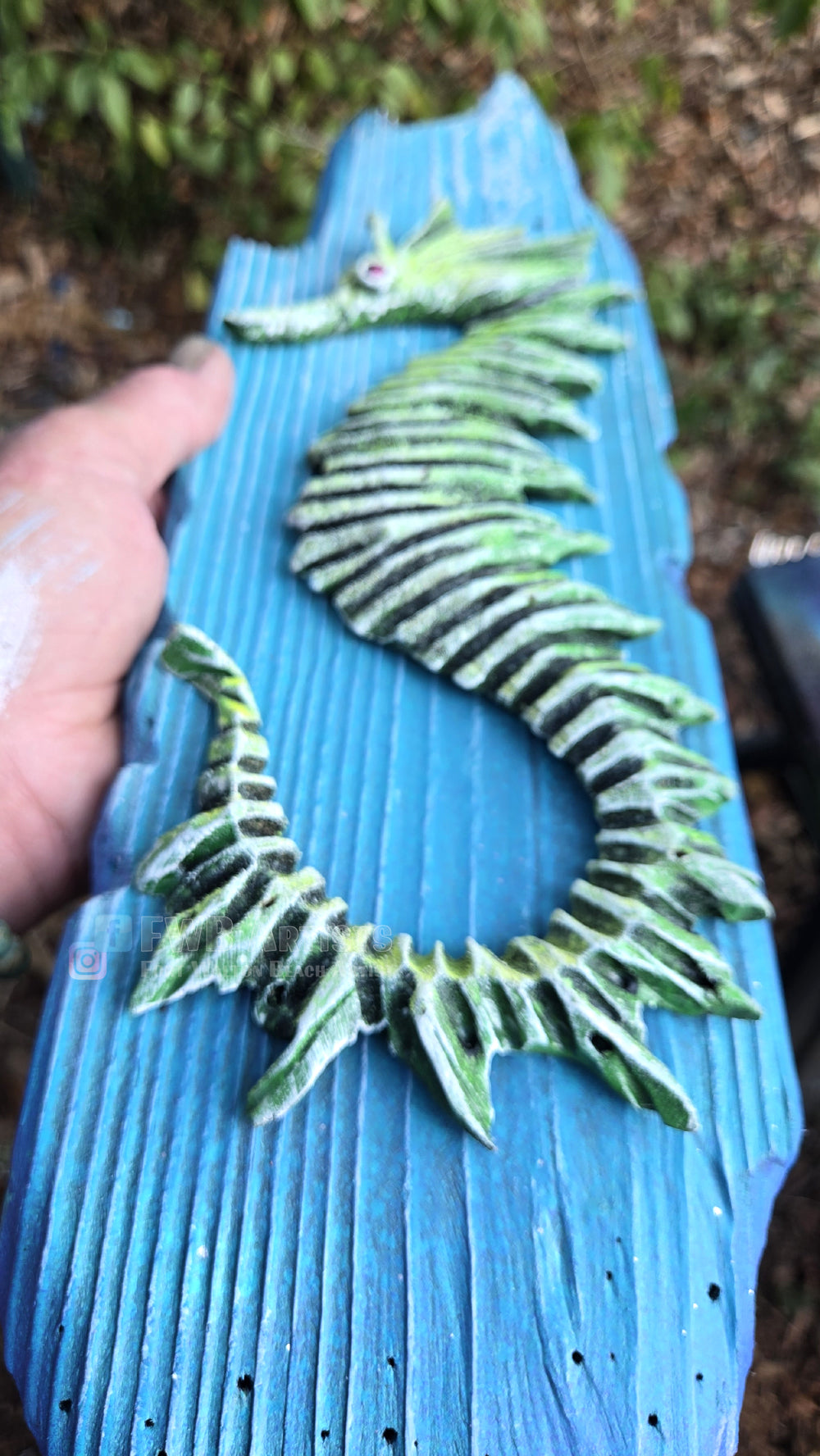 Artist's hand holds a hand carved, hand-painted wooden wall art piece featuring a green seahorse on a weathered light blue background. Handmade, one-of-a-kind up-cycled Eco-Art from locally reclaimed materials Thomas Walsh at FWB Artists.