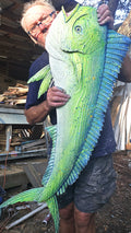 The artist at his workshop holds a large, detailed sculpture of a green and blue mahi-mahi fish.