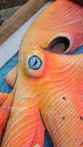 A close-up of a handcrafted highly textured orange and yellow Octopus sculpture wall art piece, featuring a prominent blue eye and natural wood grain textures.